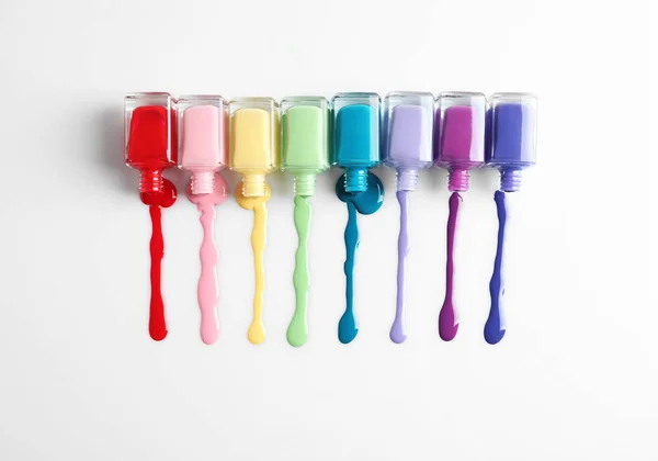 Esmaltes de uñas y botellas de colores derramados sobre fondo blanco, vista superior — Foto de Stock