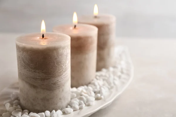 Тарелка с тремя горящими свечами и камнями на столе, место для текста — стоковое фото