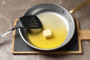 Gri masada eriyen tereyağı ve spatula ile tava, closeup
