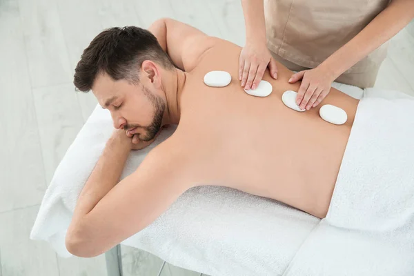 Hombre guapo recibiendo masaje de piedra caliente en el salón de spa —  Fotos de Stock