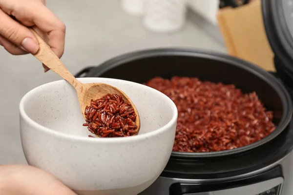 Жінка кладе коричневий рис в миску з мультиварки на кухні, крупним планом — стокове фото