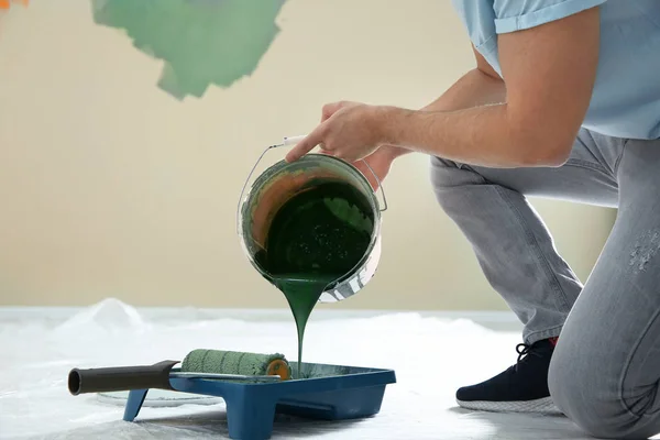 Junger Mann schüttet Farbe aus Eimer in Tablett drinnen, Nahaufnahme. Reparatur zu Hause — Stockfoto