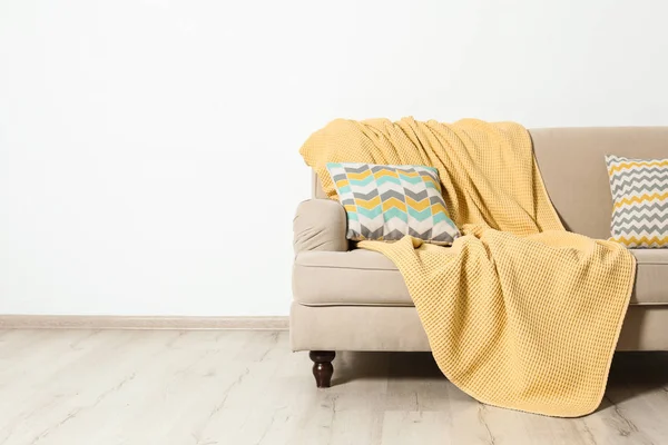 Soggiorno minimalista interno con divano, cuscini e plaid vicino alla parete luminosa. Spazio per testo — Foto Stock