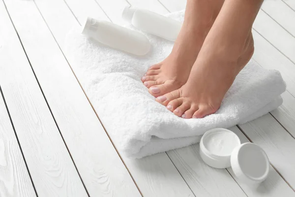 Donna con bei piedi, asciugamano e prodotti cosmetici sul pavimento in legno bianco, primo piano. Trattamento termale — Foto Stock