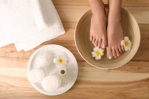 Vrouw doorweekt haar voeten in schotel met water en bloemen op houten vloer, bovenaanzicht. Kuuroord — Stockfoto