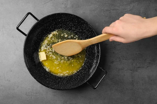 Жінка змішує тане масло на сковороді на сірому фоні, вид зверху — стокове фото