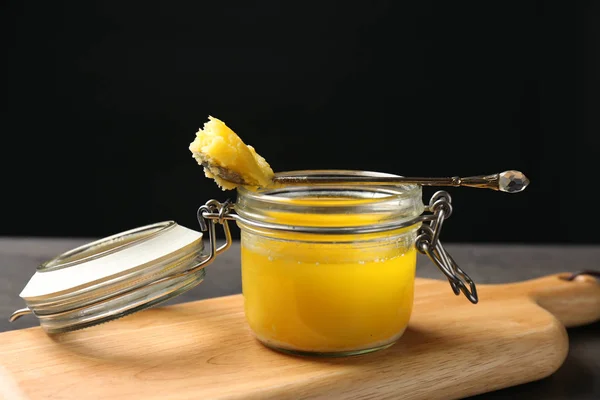 Tarro y cuchara con mantequilla clarificada sobre tabla de madera — Foto de Stock