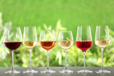 Row of glasses with different wines on grey table against blurred background clipart