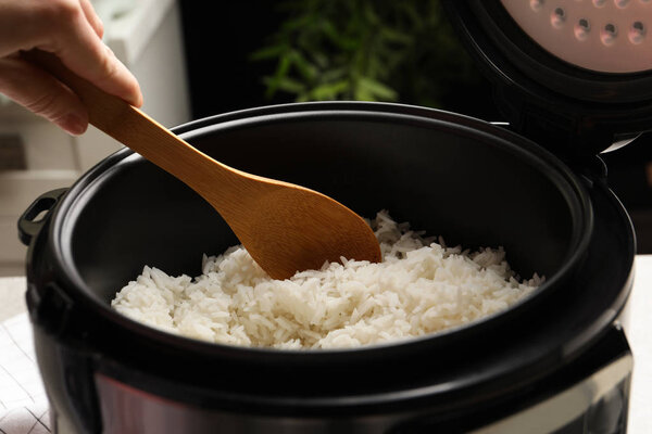 Woman taking tasty rice with spoon from cooker in kitchen, closeup