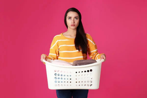 Недовольная молодая женщина держит корзину с бельем на цветном фоне — стоковое фото