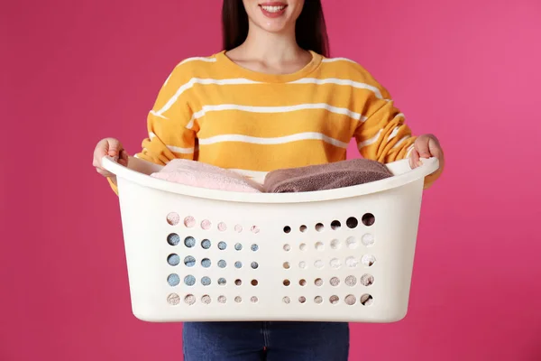 Young woman holding basket with laundry on color background, closeup