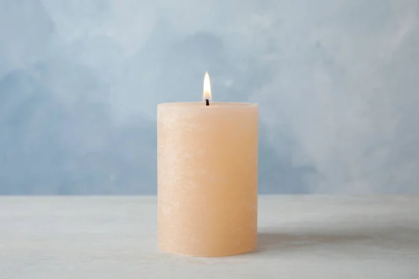 Brennende Kerze auf Tisch vor farbigem Hintergrund — Stockfoto