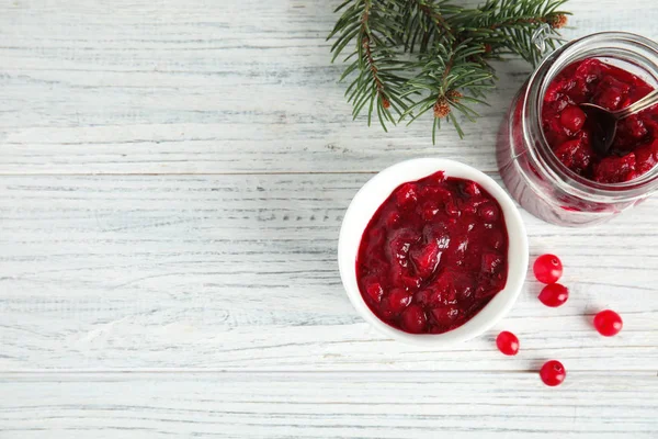 Tigela e jarra com molho de cranberry saboroso no fundo de madeira branco, leigos planos. Espaço para texto — Fotografia de Stock