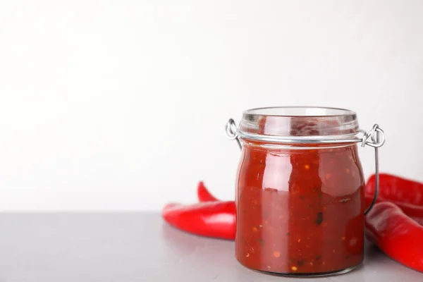 Vaso di vetro di salsa di peperoncino piccante con peperoni sul tavolo su sfondo bianco. Spazio per testo — Foto Stock