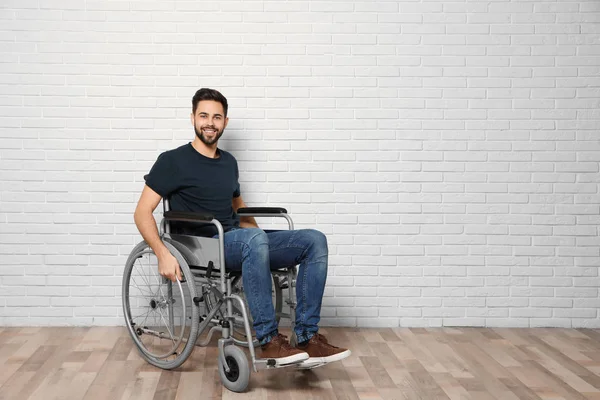 Junger Mann im Rollstuhl in der Nähe von Ziegelmauer drinnen. Raum für Text — Stockfoto