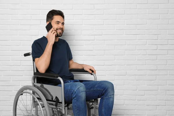 Jongeman in een rolstoel praat over de telefoon in de buurt van bakstenen muur. Ruimte voor tekst — Stockfoto