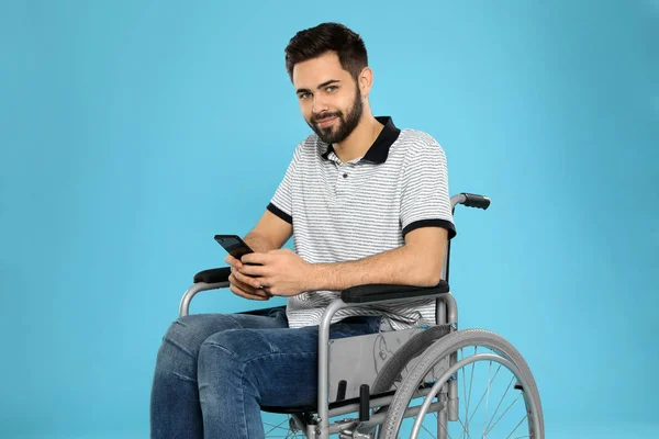 Młody człowiek ze smartfonem na wózku inwalidzkim na tle koloru — Zdjęcie stockowe
