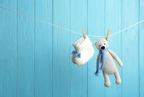 Botas de bebê e urso de brinquedo na linha de lavanderia contra fundo de madeira cor, espaço para texto. Acessórios para crianças — Fotografia de Stock