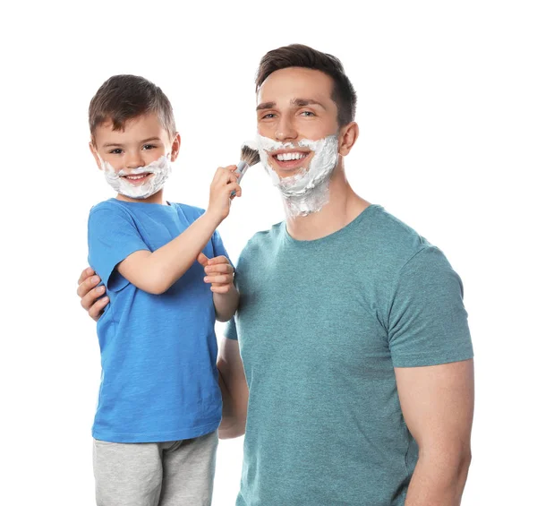 Pequeno filho aplicando espuma de barbear no rosto do pai contra o fundo branco — Fotografia de Stock