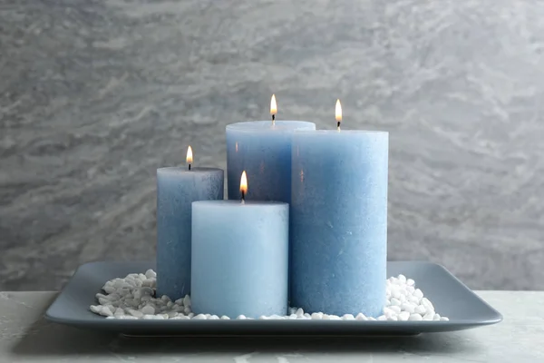 Тарелка с горящими свечами и камнями на столе — стоковое фото