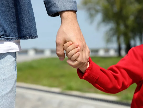 Bambino che si tiene per mano con suo padre all'aperto, primo piano. Weekend in famiglia — Foto Stock