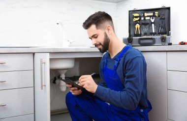 Mutfak lavabosu yakınında pano ile erkek tesisatçı. Onarım hizmeti