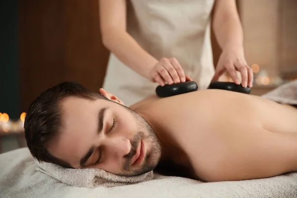Hombre guapo recibiendo masaje de piedra caliente en el salón de spa — Foto de Stock