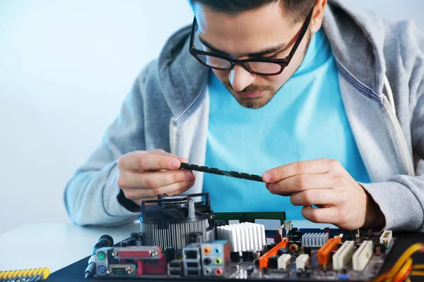 Técnico masculino reparando la placa base en la mesa contra el fondo de luz —  Fotos de Stock