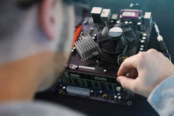 Male technician repairing motherboard at table, closeup