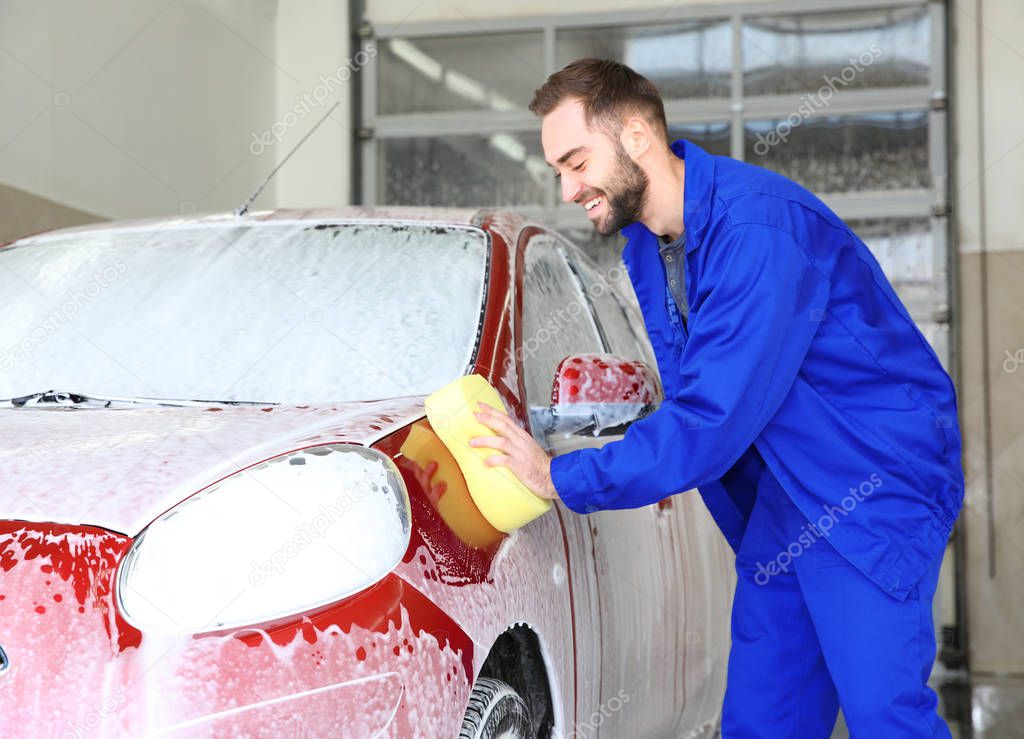 Worker cleaning automobile with sponge at professional car wash
