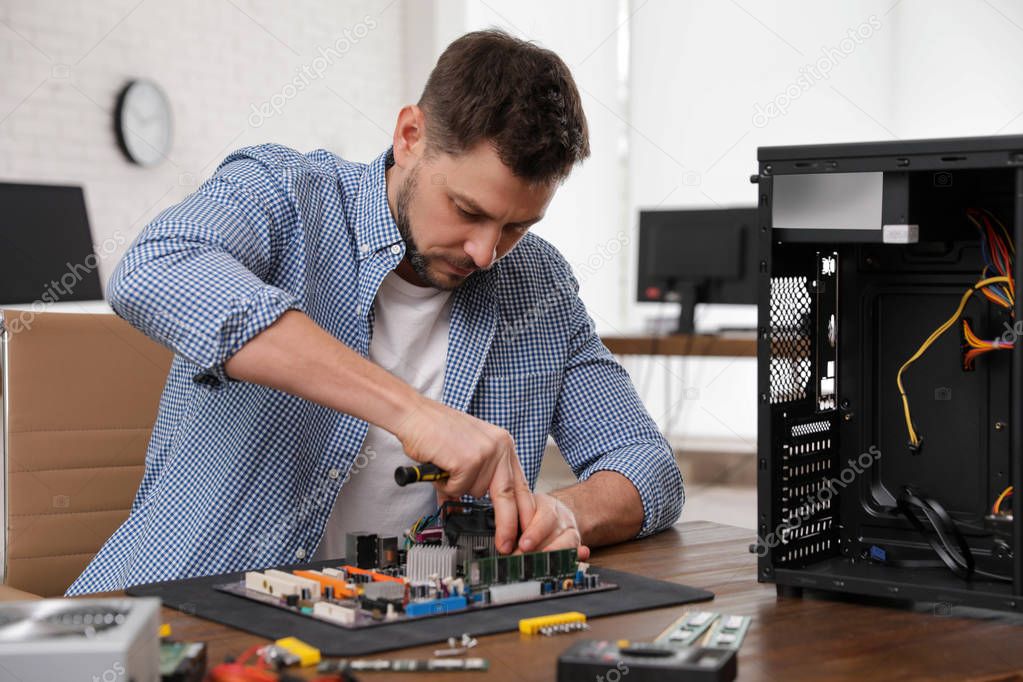 Male technician repairing motherboard at table indoors