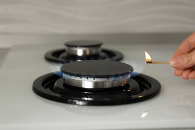 Woman lighting gas stove with match, closeup clipart