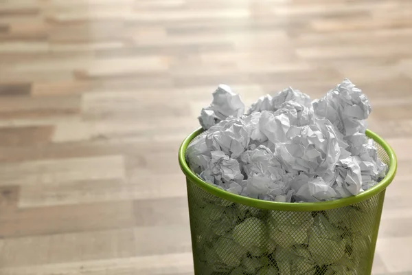 Metal bin with crumpled paper on floor, space for text