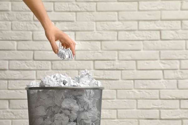 Woman throwing crumpled paper into metal bin against brick wall, closeup. Space for text