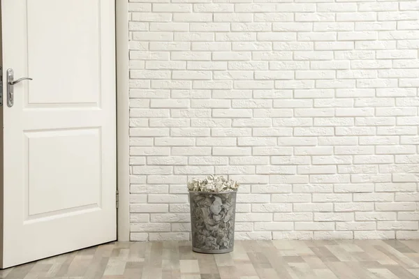 Metalen bak met verfrommeld papier op vloer tegen bakstenen muur, ruimte voor tekst — Stockfoto