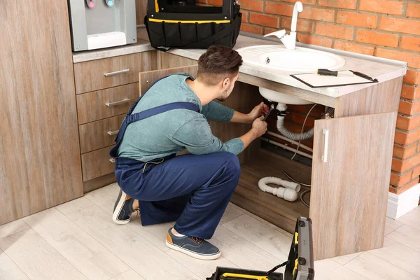 Мужчина-сантехник в форме, ремонтирует кухонную раковину — стоковое фото