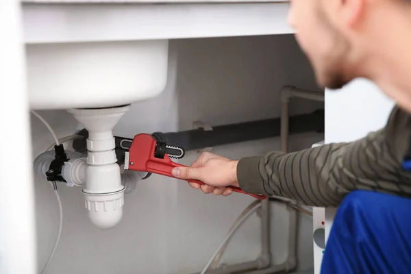 Encanador masculino reparando pia de cozinha com chave de tubo, close-up — Fotografia de Stock