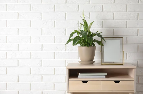 Spathiphyllum plante en pot et cadre photo sur la table près du mur de briques, espace pour le texte. Décor de maison — Photo