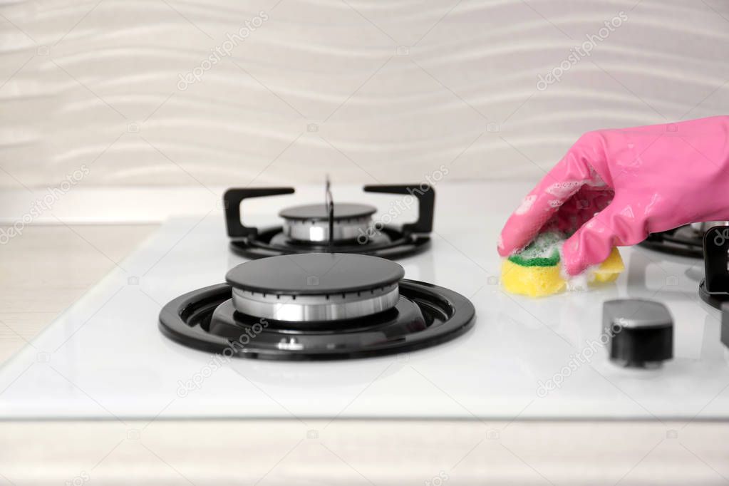 Person cleaning gas stove with sponge, closeup