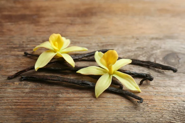 Palos de vainilla y flores sobre fondo de madera —  Fotos de Stock