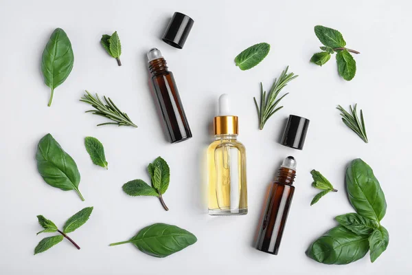 Pequenas garrafas de óleos essenciais com diferentes ervas no fundo branco, vista superior — Fotografia de Stock