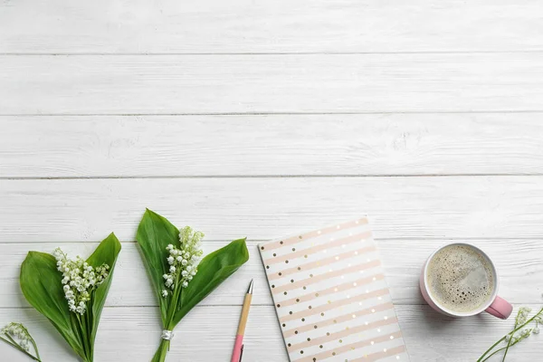 Platte lay samenstelling met notebook, lelietje van de vallei boeketten en koffie op witte houten achtergrond. Ruimte voor tekst — Stockfoto