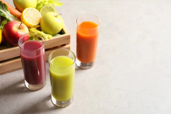 Vasos de diferentes jugos y cajón de madera con ingredientes frescos en la mesa. Espacio para texto — Foto de Stock