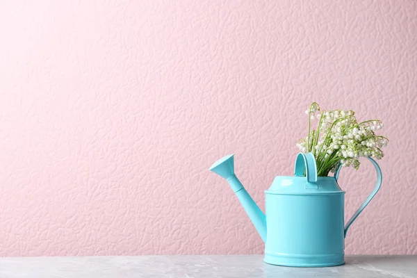 Beautiful lily of the valley bouquet in watering can on table near color wall, space for text — Stockfoto