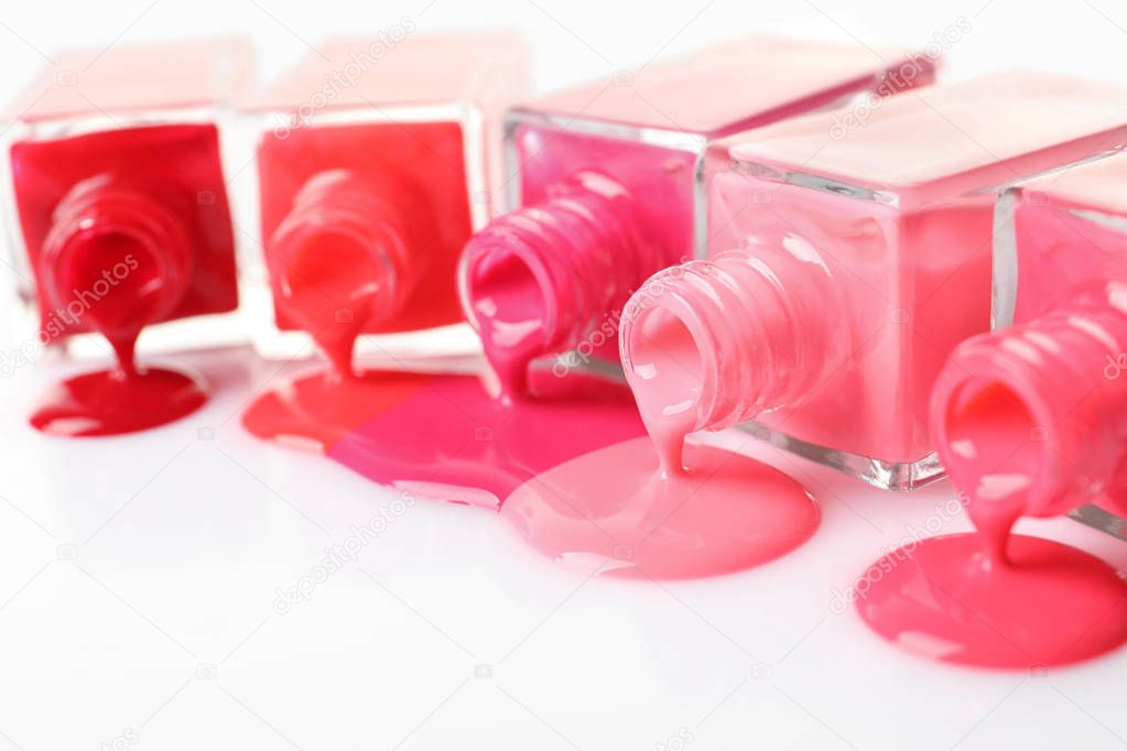 Spilled different nail polishes with bottles on white background, closeup