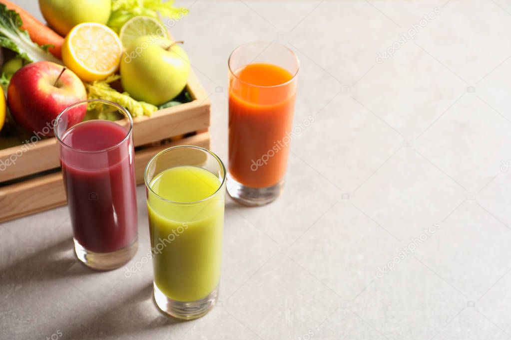 Glasses of different juices and wooden crate with fresh ingredients on table. Space for text