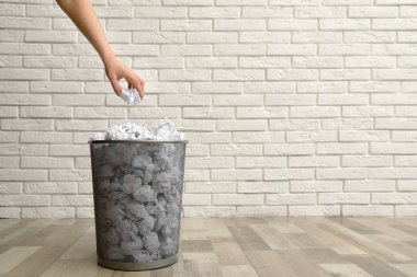 Kadının biri tuğla duvara karşı metal çöp kutusuna kağıt atıyor, yakın plan. Metin için boşluk