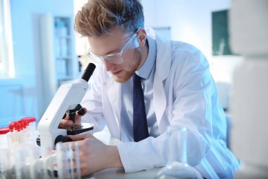 Kimya laboratuvarında modern mikroskop kullanan erkek bilim adamı