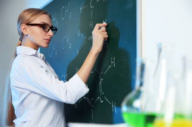 Kadın bilim adamı kapalı tebeşir tahtası üzerinde kimyasal formül yazma