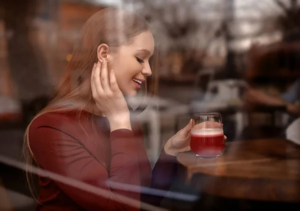 Όμορφη νεαρή γυναίκα με κοκτέιλ στο τραπέζι στο καφέ, θέα από έξω από το παράθυρο — Φωτογραφία Αρχείου